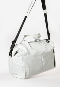 Borsa in morbida pelle grigia chiara con doppi manici e tracolla nera staccabile. Presenta una tasca con zip e una superficie morbida e texturizzata.