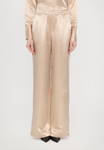 Beige satin wide-leg pants with an elastic waistband, smooth texture, and relaxed fit, paired with black pointed-toe shoes.