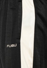 Melnas sporta bikses ar baltu strīpu pa sāniem. Priekšējā kabatas zonā ir izšūts "FUBU" logotips baltā krāsā.