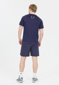 Herre atletisk tøj med en marineblå kortærmet skjorte og matchende shorts. Skjorten har et logo på ryggen; shortsene er knælange.