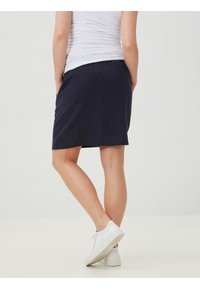 Dark blue knee-length skirt with a stretchy waistband, smooth texture, and a straight cut. Worn with white sneakers and a fitted top.