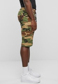 Kamuflage cargo shorts i grøn og brun, med sidelommer og elastisk talje. Kombineret med hvide sneakers og ankelstrømper.