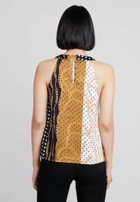 Top senza maniche con un design a blocchi di colore in nero, marrone e bianco, con motivi a pois e a catena. Tessuto morbido e dettaglio sul collo sul retro.