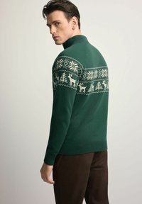 Zielony sweter dzianinowy z wzorzystą górą ozdobioną białymi płatkami śniegu, drzewami i reniferami. Wysoki kołnierz oraz ściągacze na rękawach i dole.