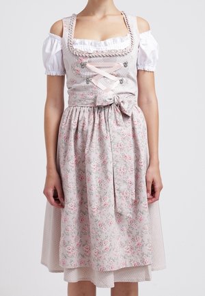 Kvinde iført en hvid skulderløs bluse under en lyserød blomsterdirndl med snørret korset og bundet forklæde i taljen.