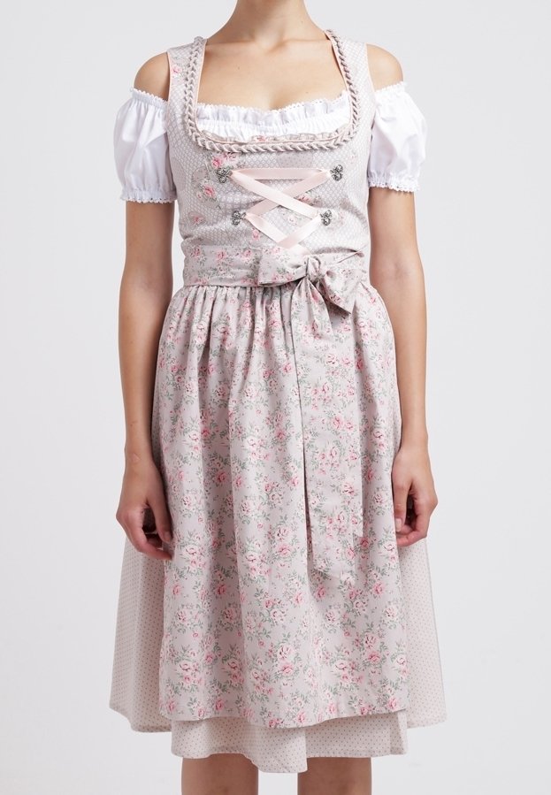 Femme portant un chemisier blanc à épaules dénudées sous une robe dirndl rose clair à motif floral, avec corsage à lacets et tablier noué à la taille.
