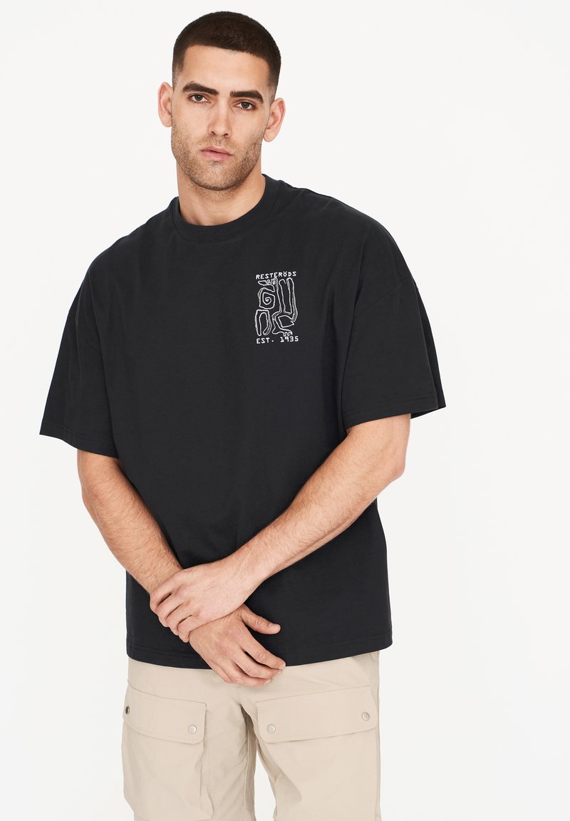 Camiseta de algodón negra con un estampado gráfico en blanco. El diseño incluye elementos abstractos y texto en la zona del pecho izquierdo.