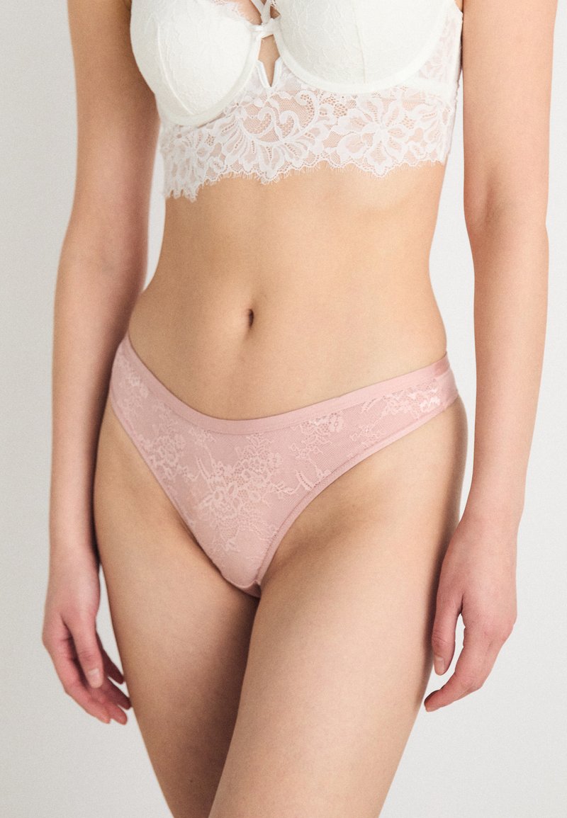 Bralette in pizzo e rete bianca con design floreale, abbinata a perizoma in pizzo rosa con una cintura liscia e intricati motivi floreali.