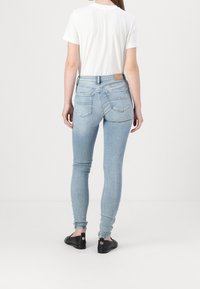 Jeans ajustados de color azul claro con una cintura alta, cuatro bolsillos, un sutil efecto de desvanecimiento y un parche de cuero marrón en la parte trasera de la cinturilla.