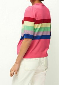 Top de punto de manga corta en color rosa con rayas horizontales multicolores, con un dobladillo acanalado y hombros abullonados, usado con pantalones blancos.