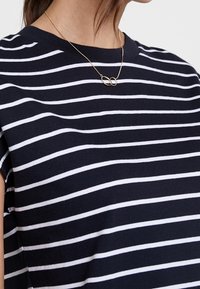 Marinrandig t-shirt med vita horisontella ränder, rundad halsringning, korta ärmar och mjukt bomullsmaterial. Guldhalsbandet framhäver.