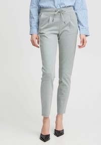 Grå stretchbyxor med dragsko i midjan, tapered design, veck framtill och slank ankellängd, tillsammans med en blårandig skjorta.
