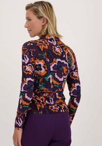 Langarmtop in een levendig bloemenpatroon van paars, oranje en groen; zachte, rekbare stof met een getailleerde snit.