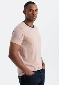 Lyserød kortærmet t-shirt med en sort ribbet halsudskæring, der har en blød tekstur og en afslappet pasform, kombineret med mørkeblå jeans.