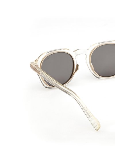 Pyöreät aurinkolasit, joissa on kirkas kehys ja tummat linssit. Sangoissa on tekstuuri, joka yhdistää läpinäkyvyyden ja metalliset yksityiskohdat.