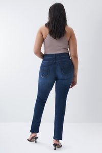 Jeans de denim de tiro alto, azul oscuro, con corte ajustado, dos bolsillos traseros y detalles de costura sutiles. Combinados con una camiseta sin mangas en un color neutro.