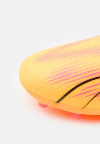 Zapatilla de fútbol de color amarillo brillante con una superficie texturizada, diseño a rayas en rosa y negro, y tacos rosas sobre una suela semi-translúcida.