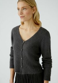 Cardigan gris à boutons, fabriqué en tissu doux et texturé, avec un col en V et de longues manches ajustées, présenté sur un fond neutre.