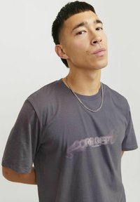 Grijze katoenen T-shirt met korte mouwen met een subtiele grafische tekstontwerp "CORE DEPT." op de voorkant, aangevuld met een zilveren ketting.