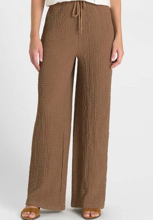 Bruine, gestructureerde wijde broek met elastische tailleband en trekkoord, gedragen met bruine sandalen met open teen.