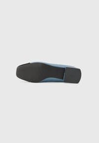 Blå platt sko med en sl�ät ovandel, fyrkantig tå och en svart texturerad sula. Har rena linjer och en minimalistisk design.