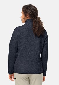 Fleece jack in marineblauw met een gestructureerd, donzig oppervlak. Hoge kraag, lange mouwen en een getailleerd ontwerp.