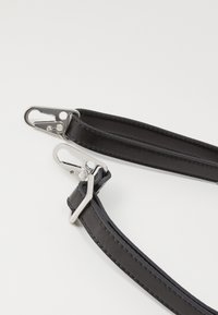 Cinghia a spalla in pelle nera con hardware in metallo argentato, dotata di due ganci e cuciture visibili lungo i bordi. Texture liscia nel complesso.