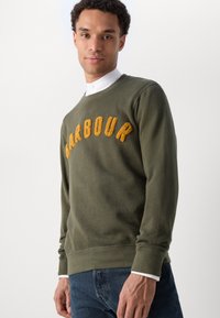 Olivově zelená mikina s texturovaným žlutým logem "BARBOUR" přes prsa, s kulatým výstřihem a ribovanými manžetami a lemem.