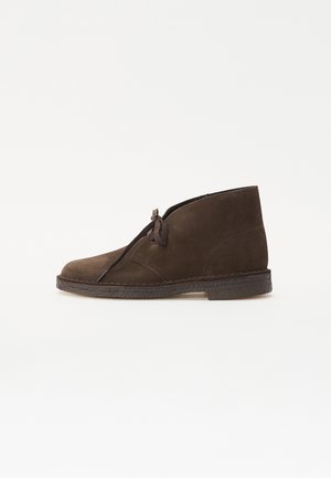 Botine din suede maro, cu vârful rotunjit, șireturi în față și talpă din cauciuc texturat. Prezintă accente cusute pe lateral.