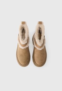 Tan nubuck ankelstøvler med blød beige kunstpelsfor, rund tå og tekstureret gummisål. Lynlås i siden for nem påklædning.