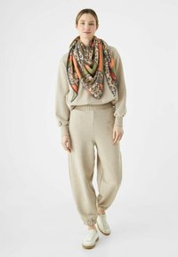 Pull oversized beige avec des poignets côtelés, jogging assorti et écharpe multicolore à motifs. Baskets blanches avec des accents beiges.