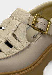 Μπεζ δερμάτινο και σουέντ σανδάλι με χρυσή τετράγωνη αγκράφα και λεπτομέρειες με ανοίγματα σε καφέ ελαστική σόλα.