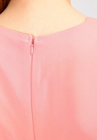 Rosa klänning med en slät textur, som har en dold dragkedja bak och en enkel, ren design av halsringningen.