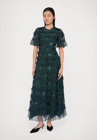 Langes, dunkelgrünes Kleid aus geschichtetem Tüll, verziert mit Pailletten und Rüschenakzenten. Enganliegendes Oberteil und kurze, rüschierte Ärmel.