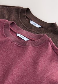 Deux sweat-shirts à col rond, l'un en bordeaux et l'autre en marron foncé, fabriqués en tissu texturé, présentés avec des étiquettes visibles.