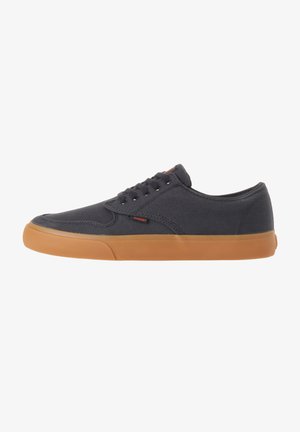 Zapatillas de lona para hombre con parte superior en gris oscuro y suela de goma. Cuentan con cordones redondos y un sutil acento de logo. Diseño de perfil bajo.