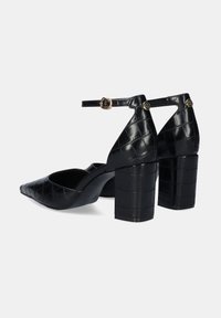 Zapatos de tacón alto de cuero sintético negro con punta afilada, correa de tobillo con herrajes metálicos y una textura de cocodrilo estampada en la superficie.