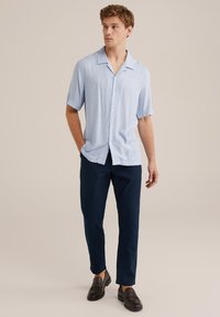 Világoskék rövidujjú ing, gombos elejével, sötétkék nadrággal és fekete slip-on cipővel párosítva. Simaságot sugalló anyagtextúra.