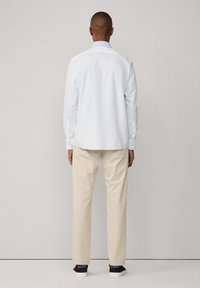 Camicia bianca a maniche lunghe con colletto blu, pantaloni beige e sneaker scure. La camicia presenta polsini con bottoni e una texture liscia.