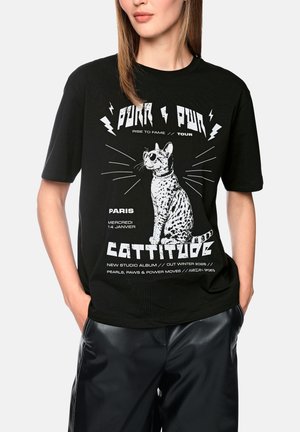 Woman wearing black t-shirt with a white graphic of a spotted cat wearing sunglasses and text about a fictional music tour and album.