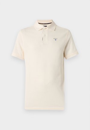 Kreemikas lühikeste varrukatega polo särk kahe nupu ja vasaku rinna piirkonnas tikitud Barbouri logoga, taustal tavaline taust.