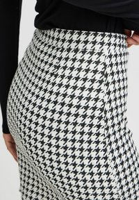 Nederdel i sort-hvid houndstooth-mønster med høj talje, glat tekstur og skræddersyet pasform, der fremhæver det geometriske kontrast gennem hele designet.
