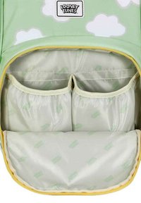 Interior de mochila verde con patrón de nubes; cuenta con dos bolsillos pequeños y un compartimento más grande, todos forrados con un material suave y de color claro.