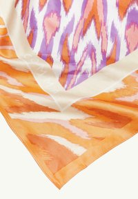 Jedwabny szalik z żywym wzorem w pomarańczowe, różowe i fioletowe zygzaki w otoczeniu kremowej ramki, która pokazuje subtelne oznakowanie.
