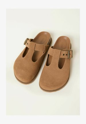 Ruskeat mokkanahkaiset liukusäädettävät puukengät, joissa on leikatut kuviot ja säädettävä hihna. Varustettu pehmustetulla sisäpohjalla ja kuvioidulla kumipohjalla.