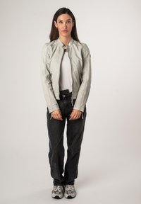 Giacca di pelle grigia chiara con colletto rialzato, chiusura con zip e jeans neri. Sneakers grigie e nere completano l'outfit.