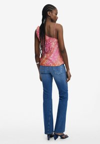 Rosa och orange mönstrad axelbandslös topp parat med blå utsvängda jeans och blå klackar. Mjuk tyg med ett svävande mönster och justerbara axelremmar.