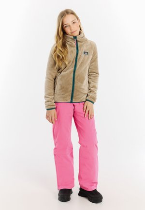 Beige fleece jack met hoge kraag en teal rits, gecombineerd met felroze waterdichte broek en zwarte laarzen, op een witte achtergrond.