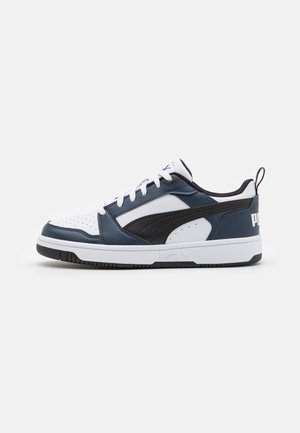 Baskets basses à tige blanche, empiècements bleu marine et noirs, lacets blancs, accents noirs sur la semelle et logo Puma au talon et sur le côté.
