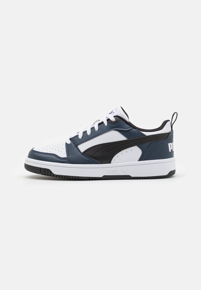 Baskets basses à tige blanche, empiècements bleu marine et noirs, lacets blancs, accents noirs sur la semelle et logo Puma au talon et sur le côté.